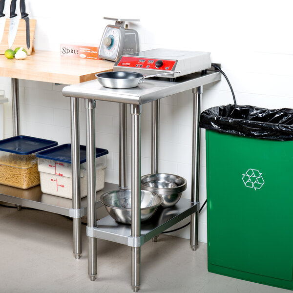 An Advance Tabco stainless steel filler table with a backsplash and undershelf in a kitchen with a green garbage can and a table.