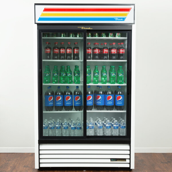A white True refrigerated glass door merchandiser with a display of soda and water bottles.