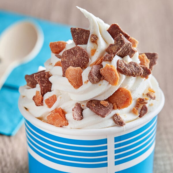A cup of ice cream with whipped cream, chocolate chunks, and chopped Butterfinger pieces.