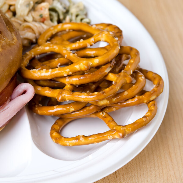 A plate with a sandwich and Snyder's of Hanover Thin Pretzels on a table.
