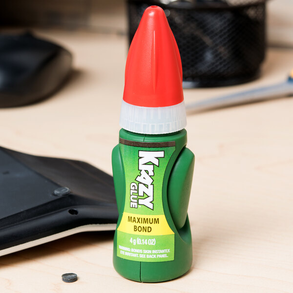 A green Krazy Glue EZ Squeeze bottle with a red cap on top of a black and white keyboard.