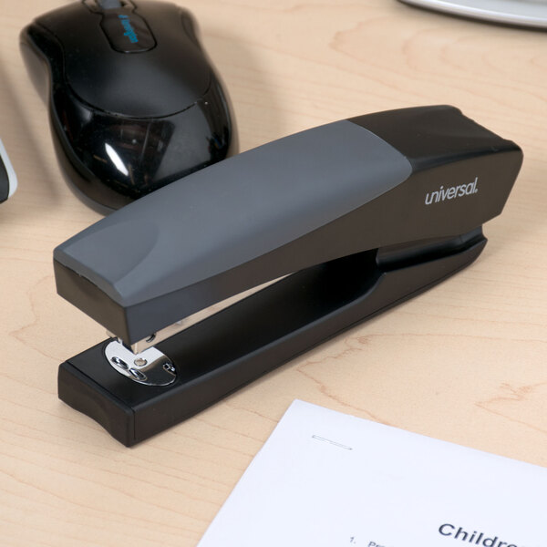 A black Universal stand up stapler on a table next to a computer mouse.