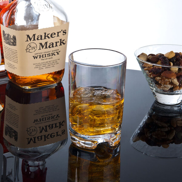 A GET SAN plastic double rocks glass filled with whiskey on the rocks on a table with a bowl of nuts.