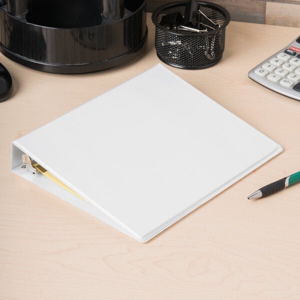 An Avery white mini binder with 1" round rings on a white desk with a pen and calculator.