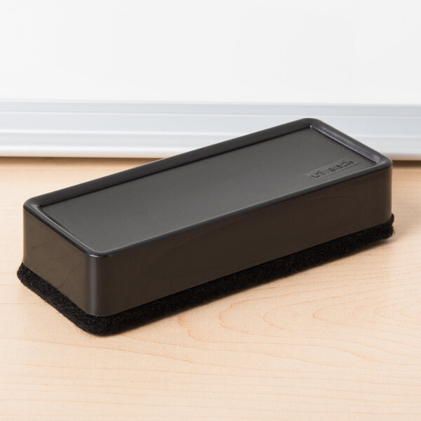 A black rectangular Universal synthetic wool felt dry erase eraser on a wood surface.