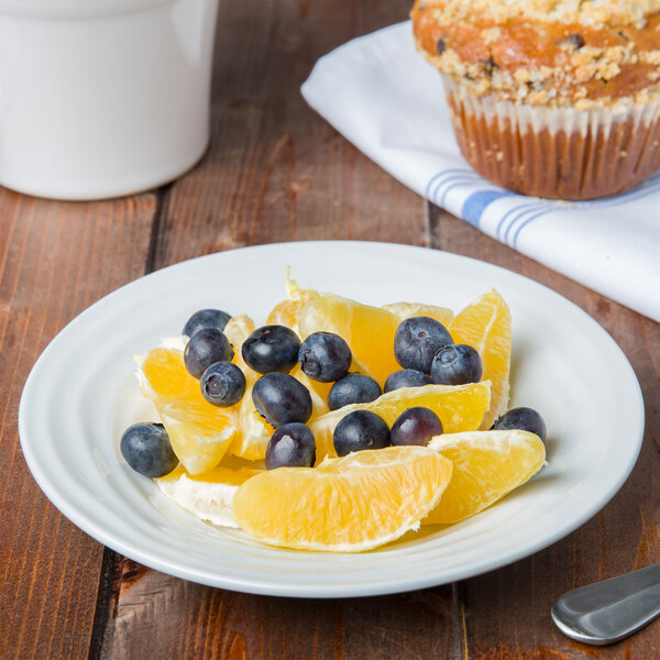 A Tuxton bright white china fruit dish with blueberries and orange slices on a table with a muffin.