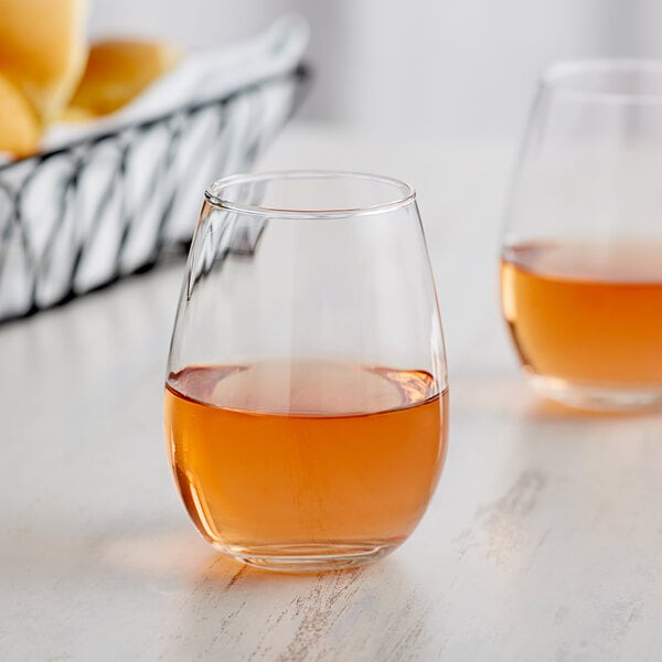 Two Acopa stemless wine glasses filled with liquid on a table.