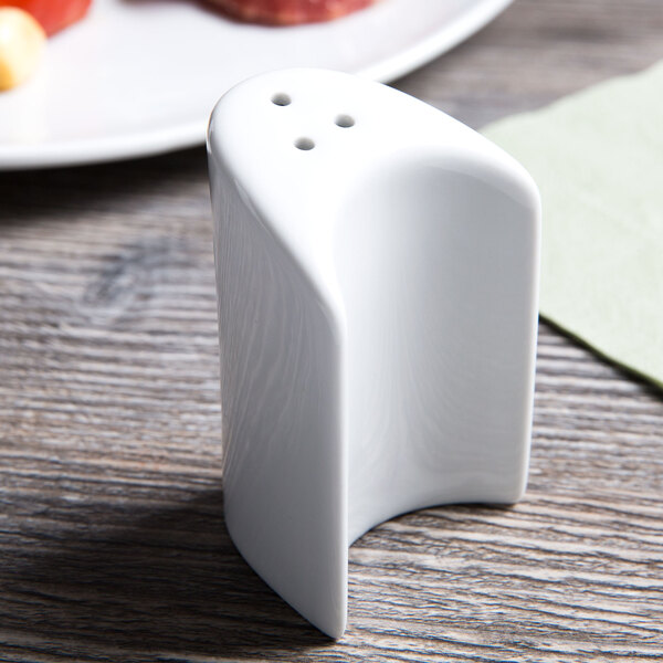 A Tuxton bright white china pepper shaker on a wood table.