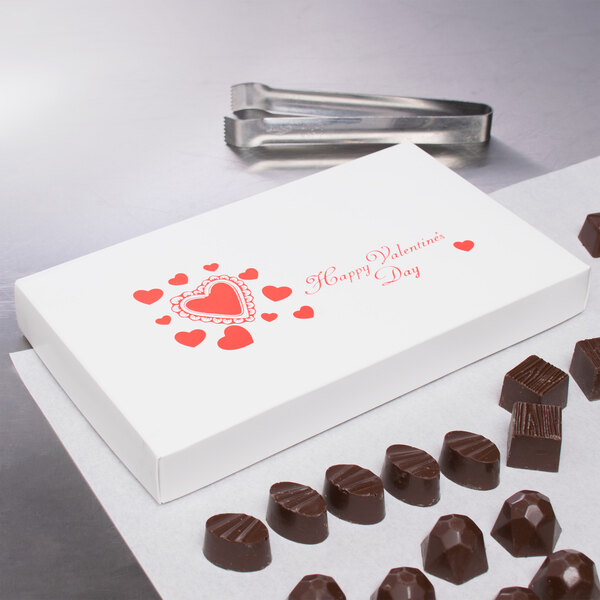 A white 2-piece Valentine's Day candy box with red hearts on a counter.