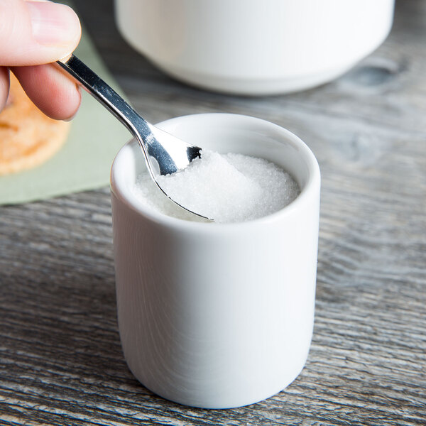 A Tuxton TuxTrendz bright white china sugar caddy with a spoon in a white cup of sugar.