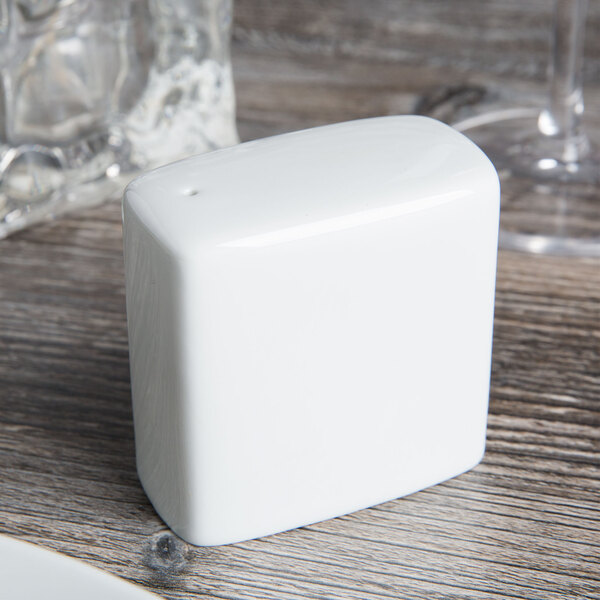 A white square Tuxton salt shaker on a wood surface.