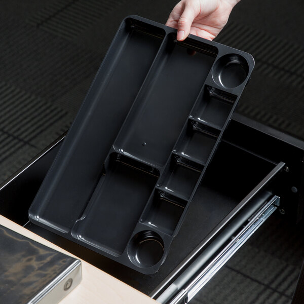 A hand holding a black Universal plastic drawer organizer with nine sections.