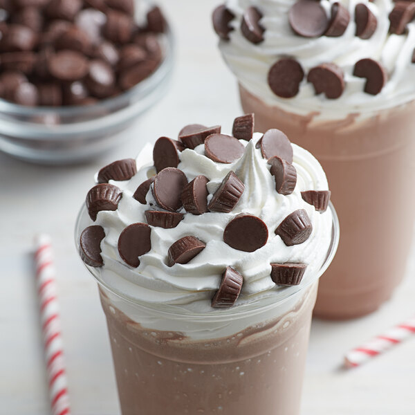 A chocolate milkshake with whipped cream and chocolate candies and a chocolate milkshake with whipped cream and chocolate chips.