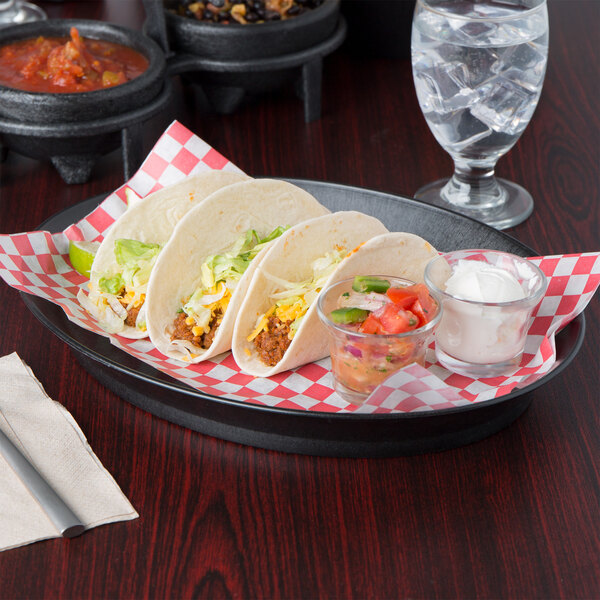 A plate of tacos on a HS Inc. oval deli server on a table with a bowl of red sauce and a glass of clear liquid.