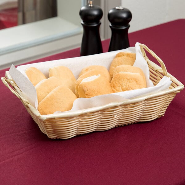 A rectangular woven basket with handles filled with bread on a table.
