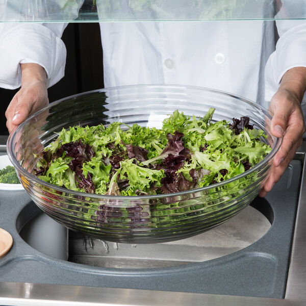 A person holding a Cambro clear round ribbed bowl filled with lettuce.