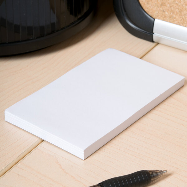A white Universal unruled scratch pad on a wood surface with a pen.