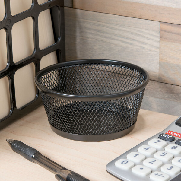 A Universal black mesh jumbo storage dish on a desk with a calculator and pen.