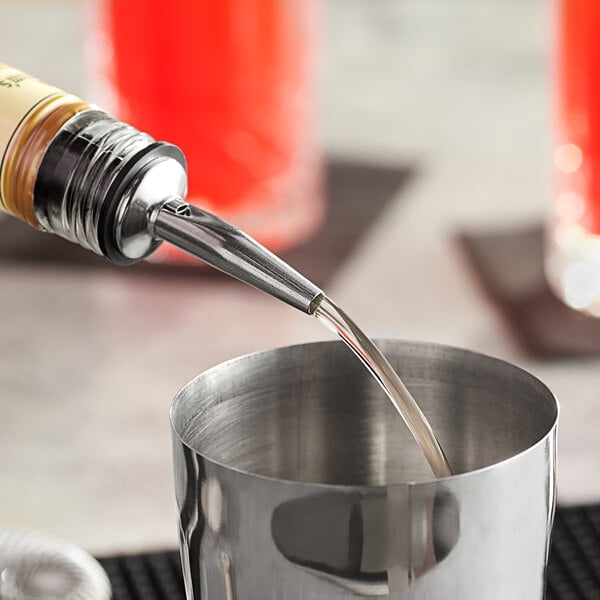 A person using an Acopa stainless steel liquor pourer to pour liquid into a cup.