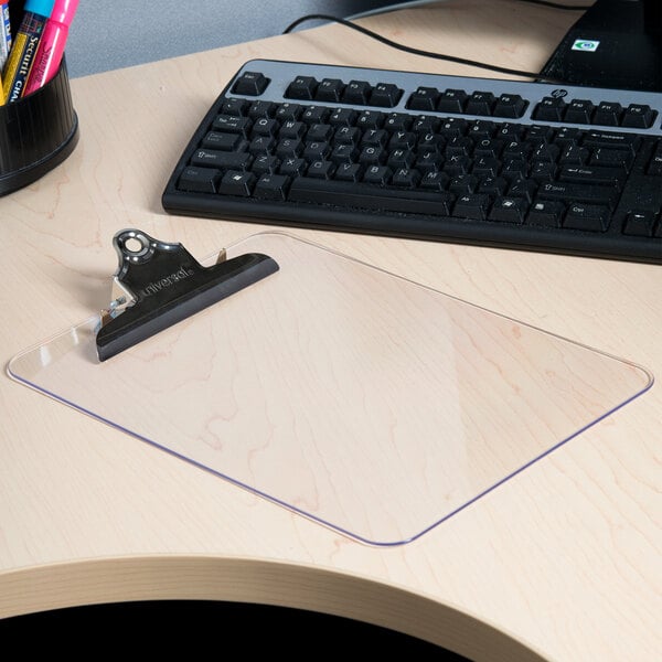 A Universal clear high capacity plastic clipboard on a wood table with a black keyboard.