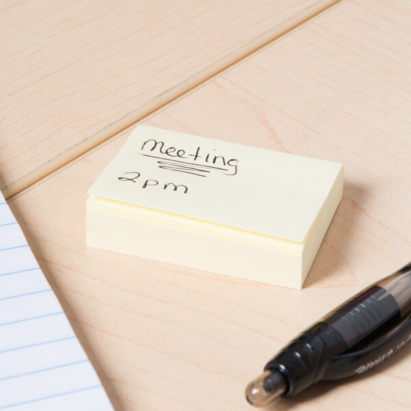A white notepad with yellow self-stick notes on it, one with black writing on it, and a black pen.
