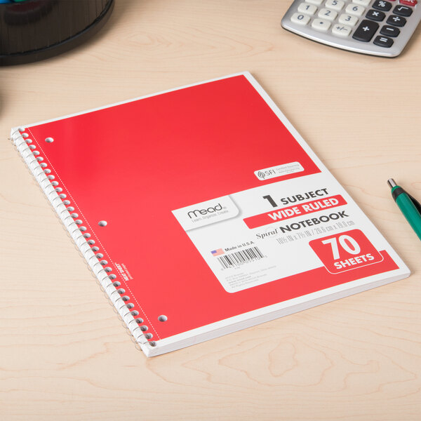 A red Mead 1 subject notebook on a wood surface with a pen.