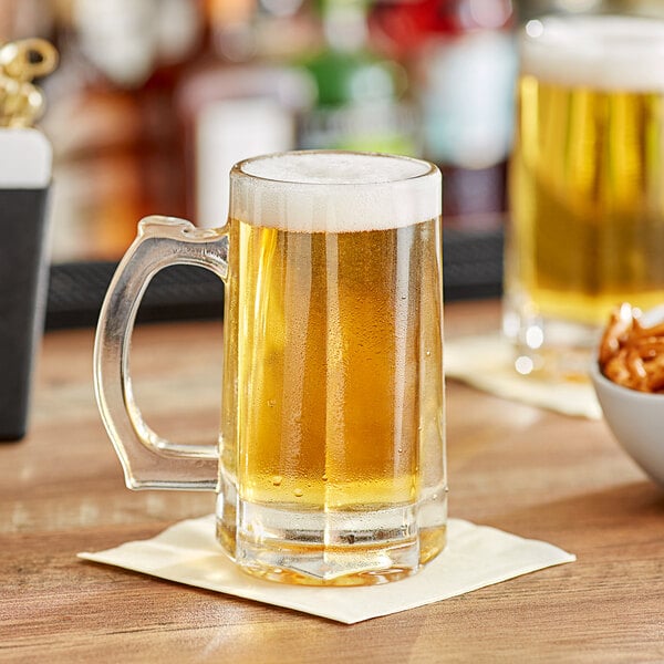 Two Acopa beer mugs filled with beer on a table.