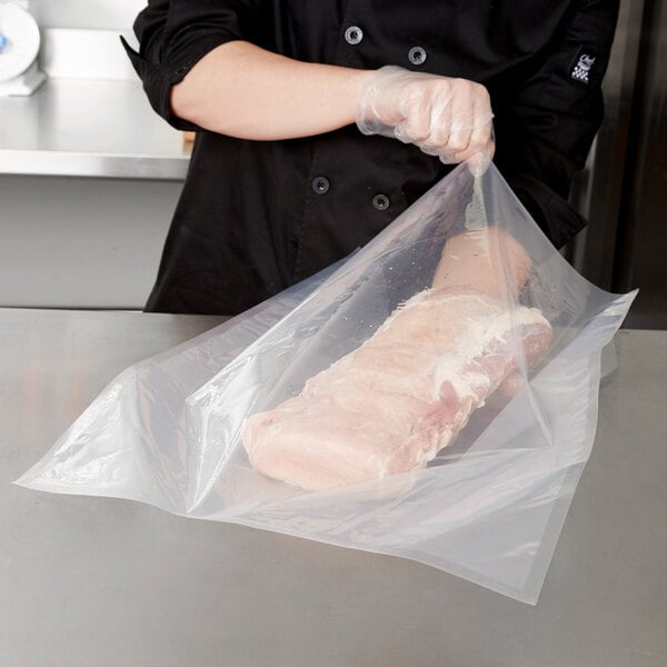 A person in a chef's uniform using an ARY VacMaster vacuum packaging bag to hold a piece of meat.