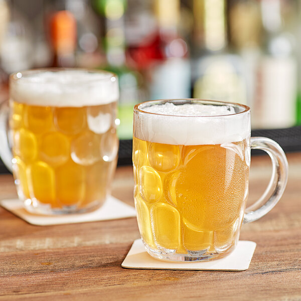 Two Acopa dimple beer mugs filled with foamy beer on a wooden table.