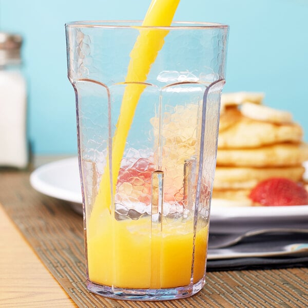 A Cambro clear plastic tumbler filled with orange juice and a straw.