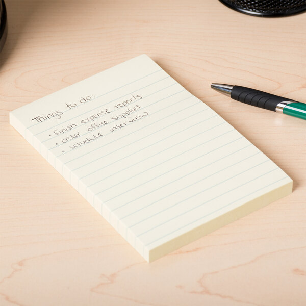 A Universal yellow ruled sticky note pad with writing on it and a pen on a desk.