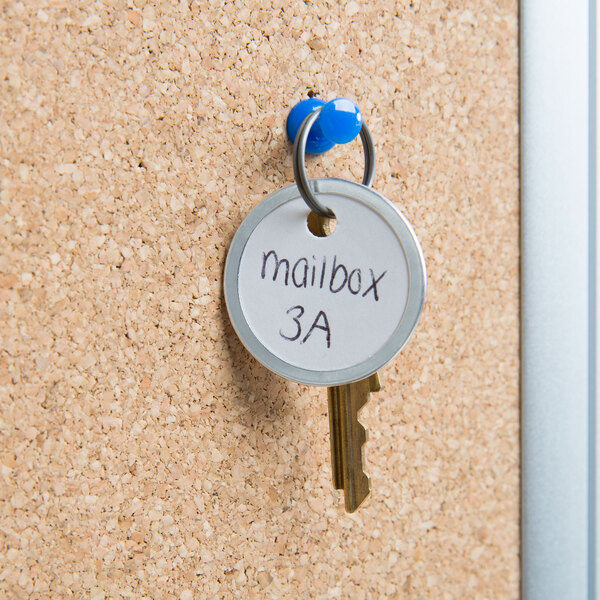 A white Avery metal rim key tag holding a mailbox key on a cork board.