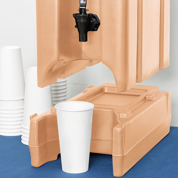 A beige plastic riser with a cup next to a Cambro insulated beverage dispenser.
