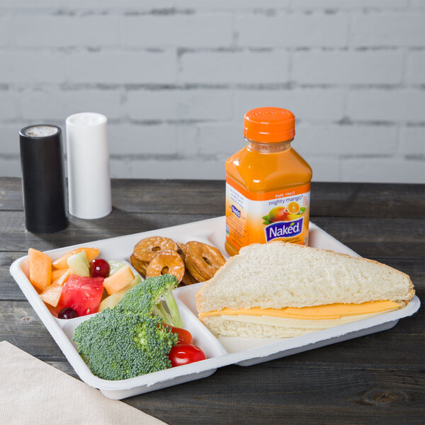 A Huhtamaki Chinet white molded fiber tray with a sandwich, fruit, and a bottle of juice on it.