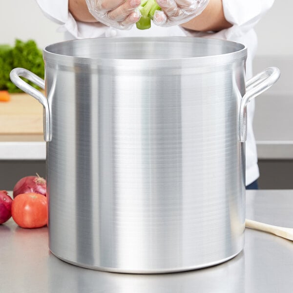 A woman using a Vollrath Wear-Ever aluminum stock pot to cook green vegetables.
