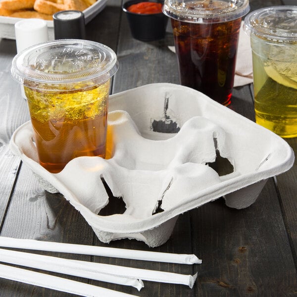 A Huhtamaki 4 cup carrier with 4 plastic cups and straws on a table.