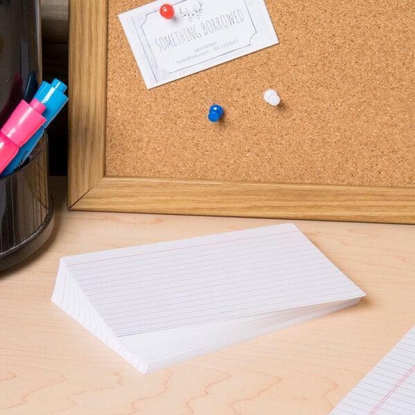 A cork board with Universal white ruled index cards on it.
