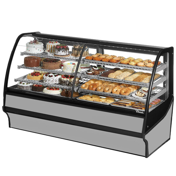 A True dual service refrigerated bakery display case with curved glass and stainless steel interior filled with different types of cakes.