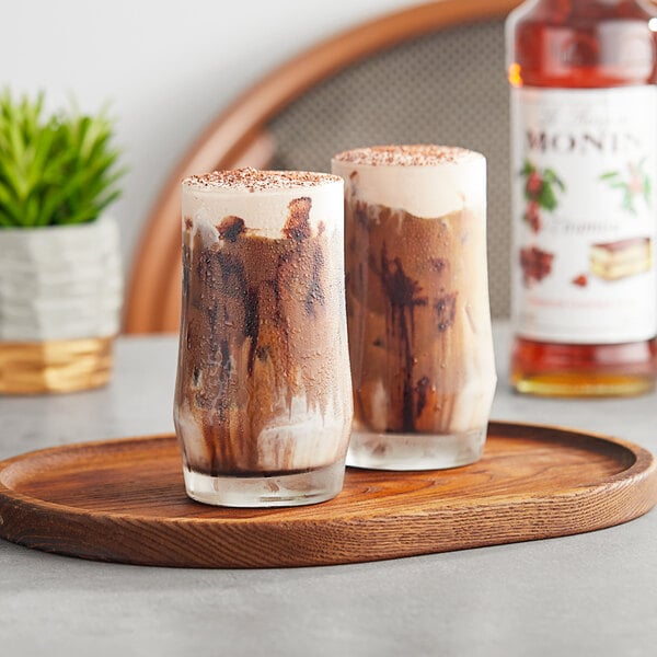 A glass of Monin Tiramisu flavoring syrup on a wooden tray with two chocolate milkshakes.