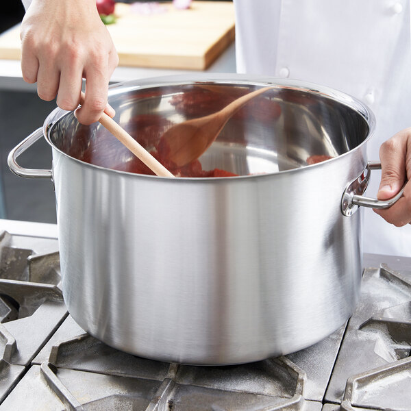A chef stirring soup in a Vollrath silver sauce pot.
