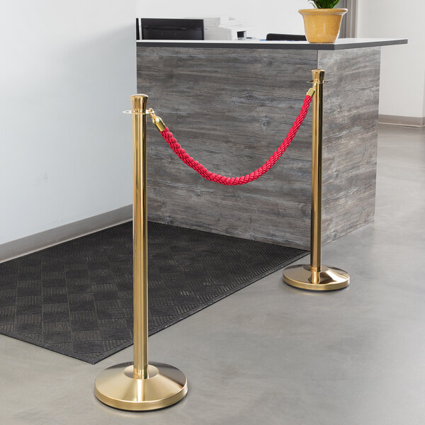 A Lancaster Table & Seating red braided rope with gold ends tied to a crowd control stanchion.