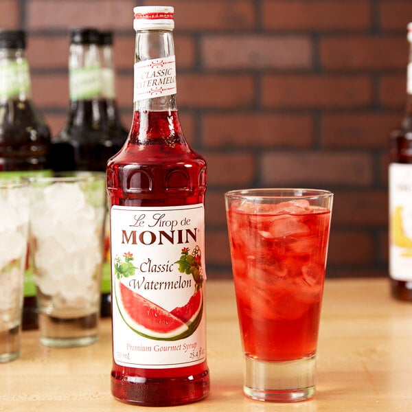 A bottle of Monin Premium Classic Watermelon Flavoring syrup next to a glass of watermelon soda.