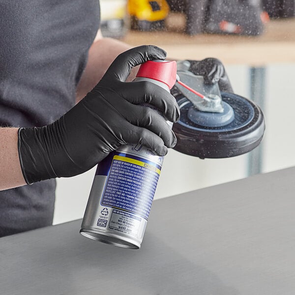 A person wearing black Lavex nitrile gloves holding a can of spray.