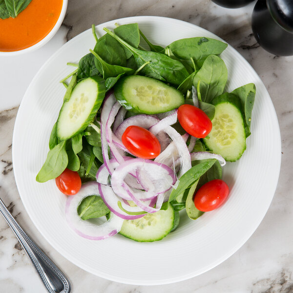 A white wide rim porcelain plate with a salad of cucumbers, tomatoes, and onions.
