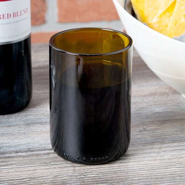An Arcoroc amber wine tumbler filled with brown liquid next to a bowl of chips.