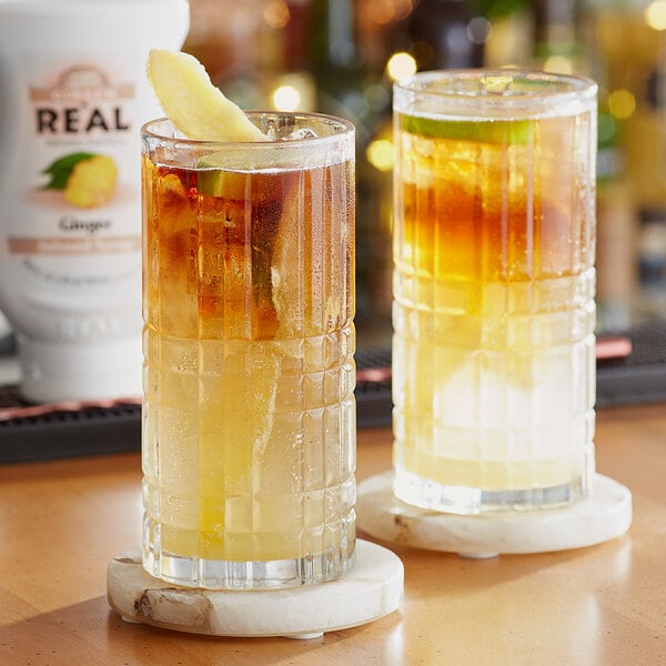 Two glasses of ginger-infused syrup over ice on a table.