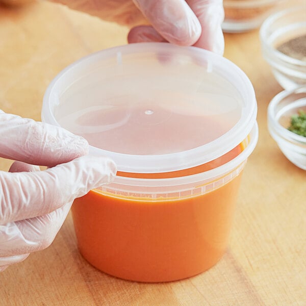 A person in gloves holding a ChoiceHD translucent plastic deli container with a lid.