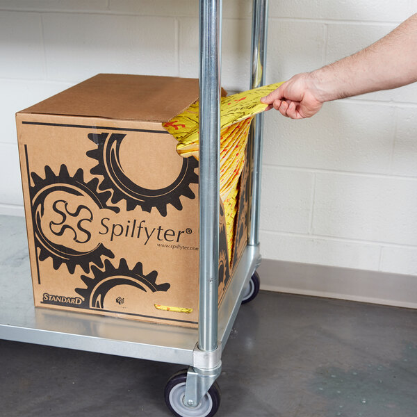 A hand pulling a yellow bag of Spilfyter HVU-75 absorbent pads out of a cardboard box.
