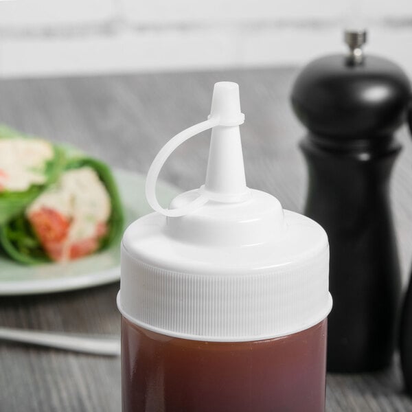 A white Tablecraft squeeze bottle of sauce with a white cap next to a plate of food.