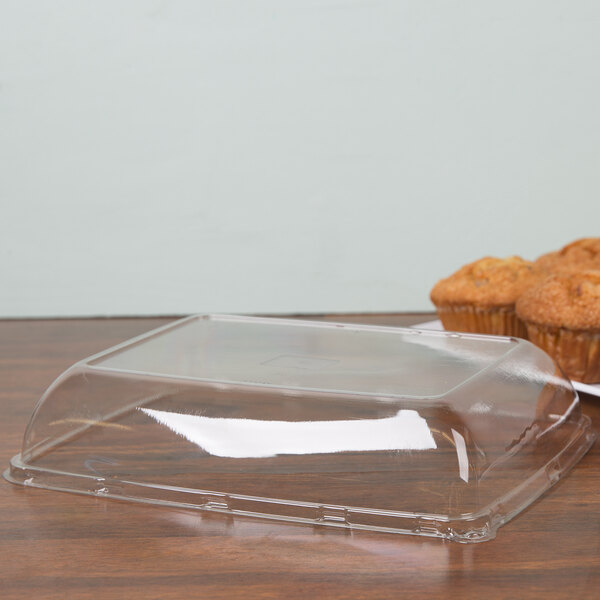 A clear plastic Sabert catering tray with a lid on a wood surface with muffins inside.